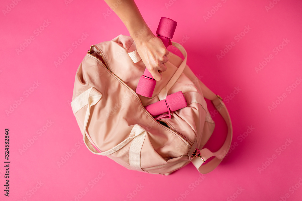 Women sports bag with dumbbells lying on pink background