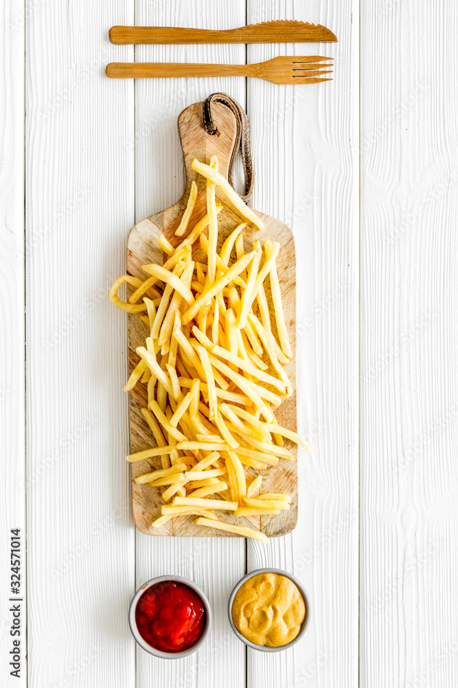 Fast food restaurant concept. French fries on cutting board near sauces on white wooden table top-do