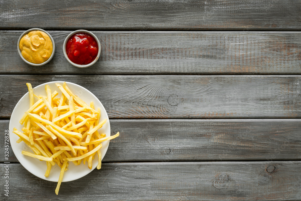 Potato chips on plate near sauces on dark wooden table top-down copy space