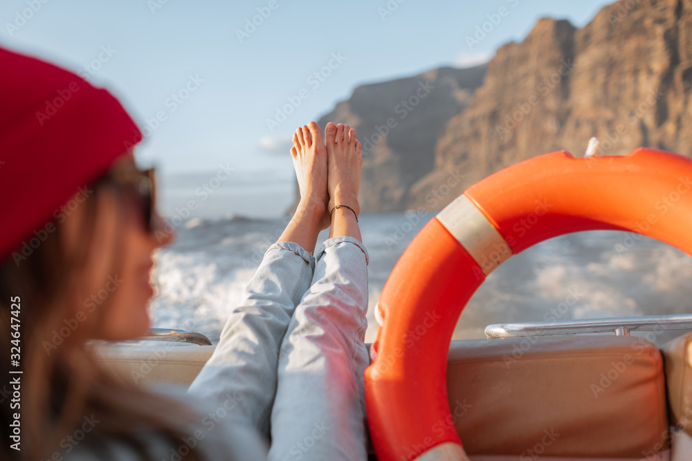 Young woman with lifebuoy enjoying sea voyage, sailing on a yacht near a rocky shore. Concept of a c