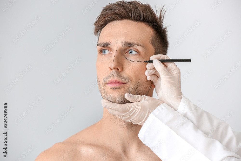 Plastic surgeon applying marking on male face against light background