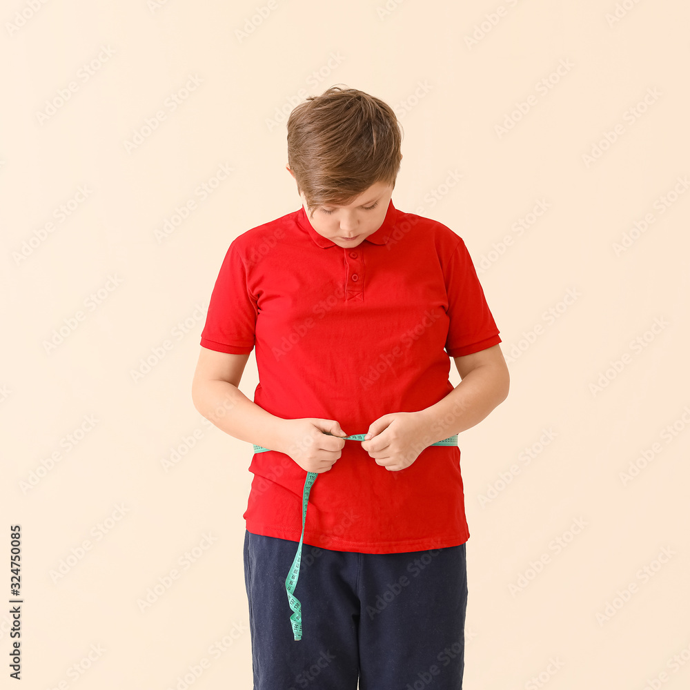 Overweight boy measuring his waist on light background