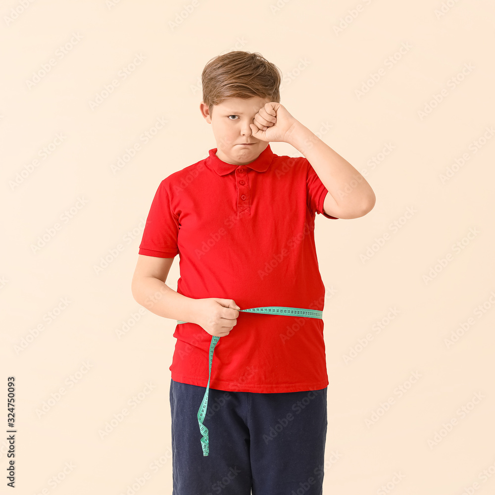 Sad overweight boy measuring his waist on light background