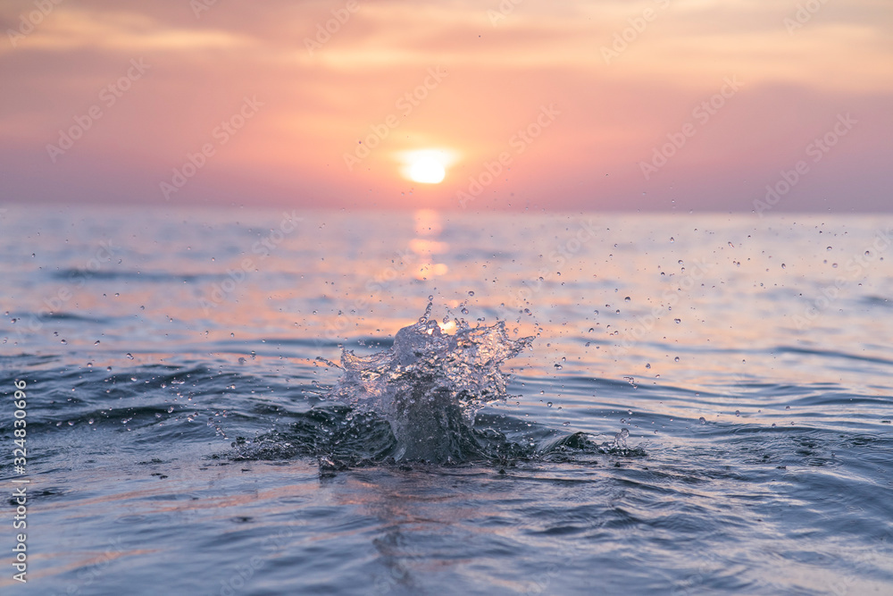 blue water splash on beautiful purple warm sunset with clouds just over the water. Perfect view for 