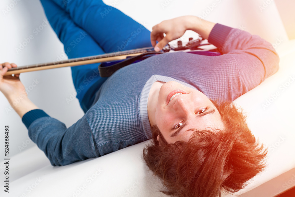 Happy young man lying back on sofa with guitar