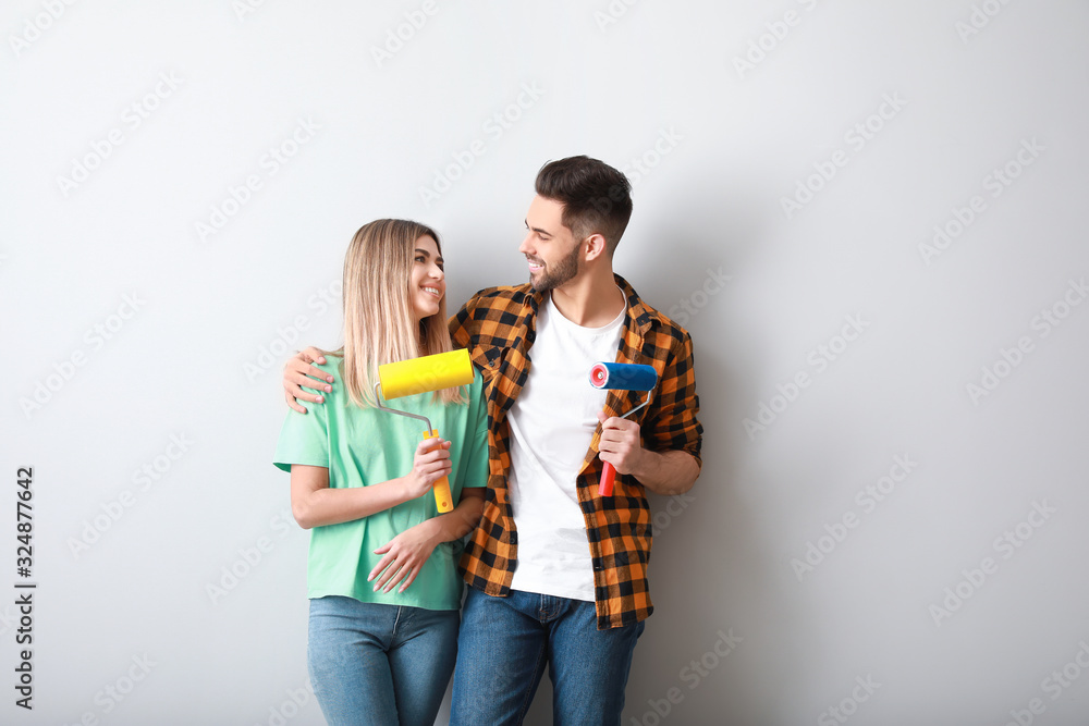 Young couple with paint rollers near light wall in new apartment