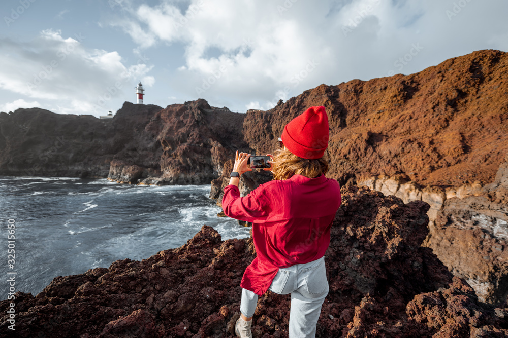 Woman photographing on phone great views on the rocky ocean coast, traveling on the Teno cape on the