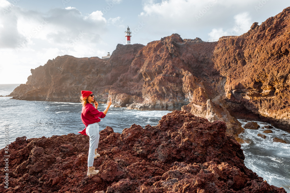 Woman enjoying great views on the rocky ocean coast and a lighthouse on the background, traveling on