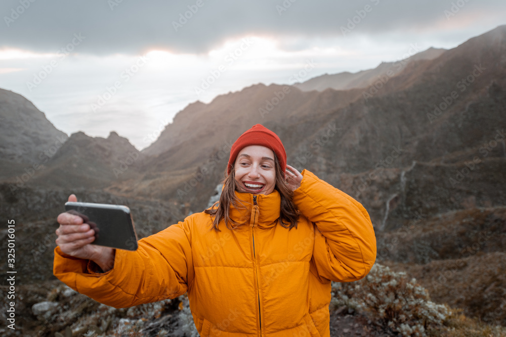 Portrait of a young traveler dressed in bright jacket and hat enjoying a trip highly in the mountain