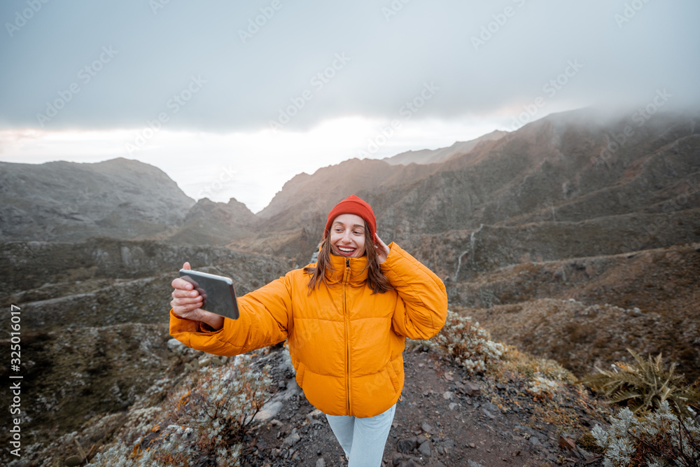 一位年轻旅行者穿着鲜艳的夹克，戴着帽子，在高山上享受旅行的肖像