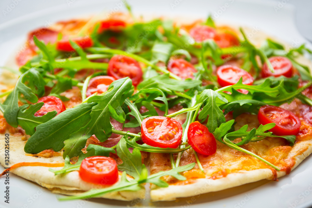 Italian pizza with rocket salad, cherry tomatoes, ham and cheese