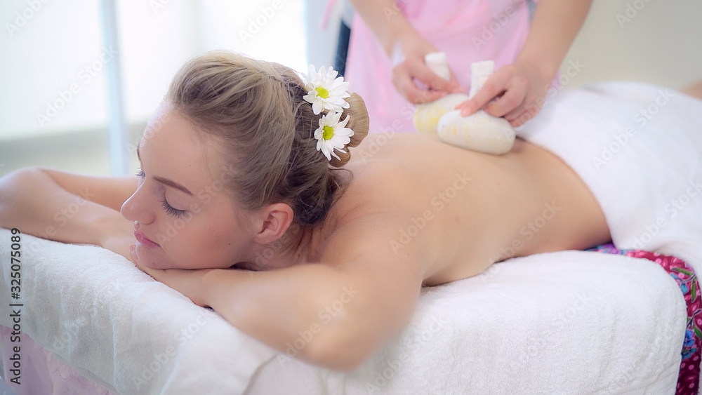 Massage therapist holds a herbal compress to do treatment to woman lying on spa bed in a luxury spa 