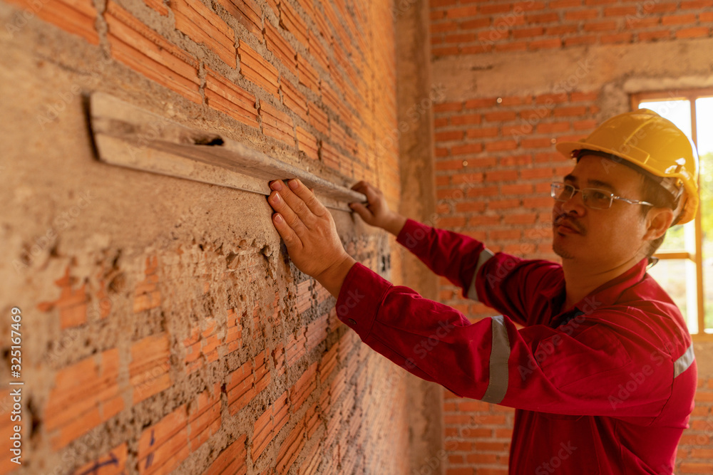 Plasterer in red working uniform plastering the wall indoors.