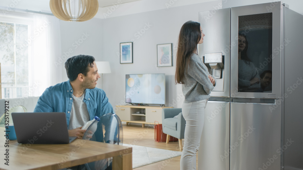 Beautiful Young Couple Drink Morning Coffee in the Kitchen. Girl Checks the Weather Forecast and a T