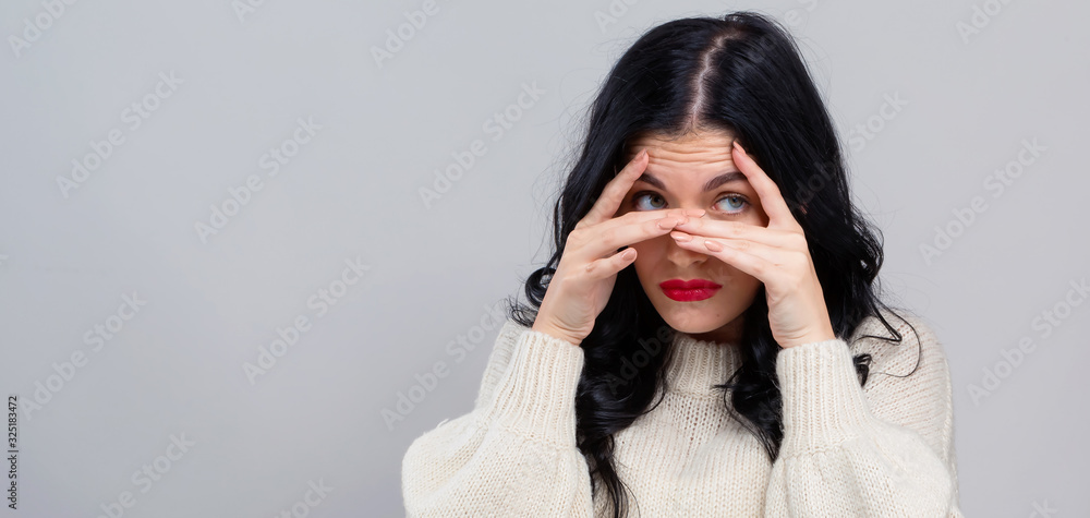 Young woman peeking though her fingers on a gray background