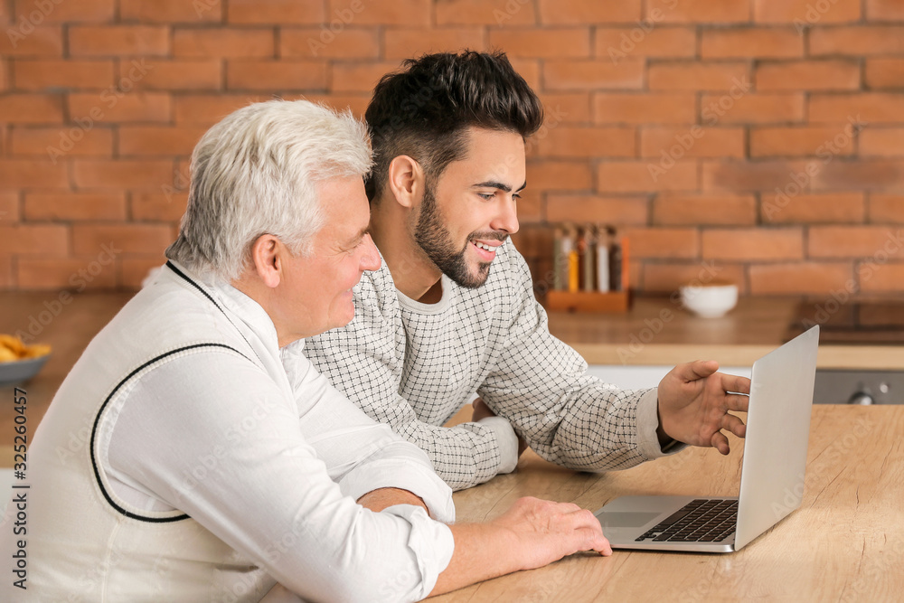 Young man and his father with laptop in kitchen