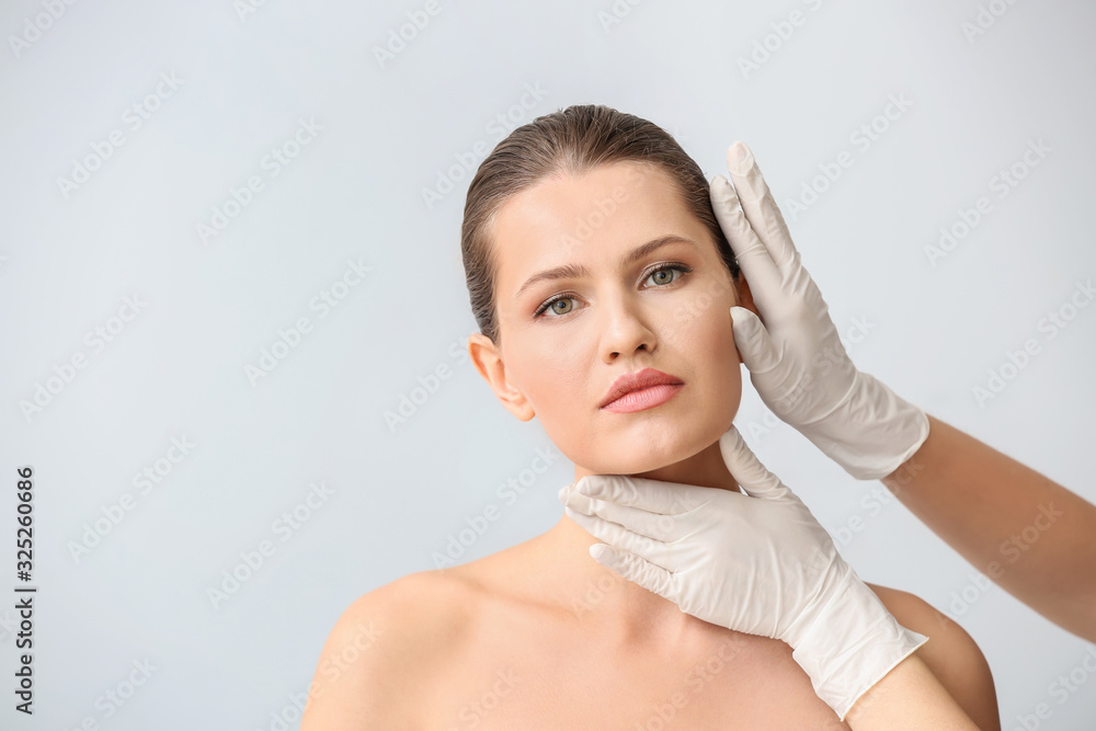 Plastic surgeon touching face of young woman against light background