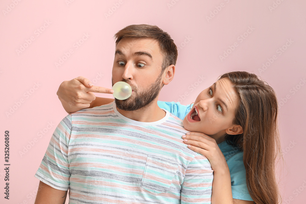 Funny young couple with chewing gum on color background