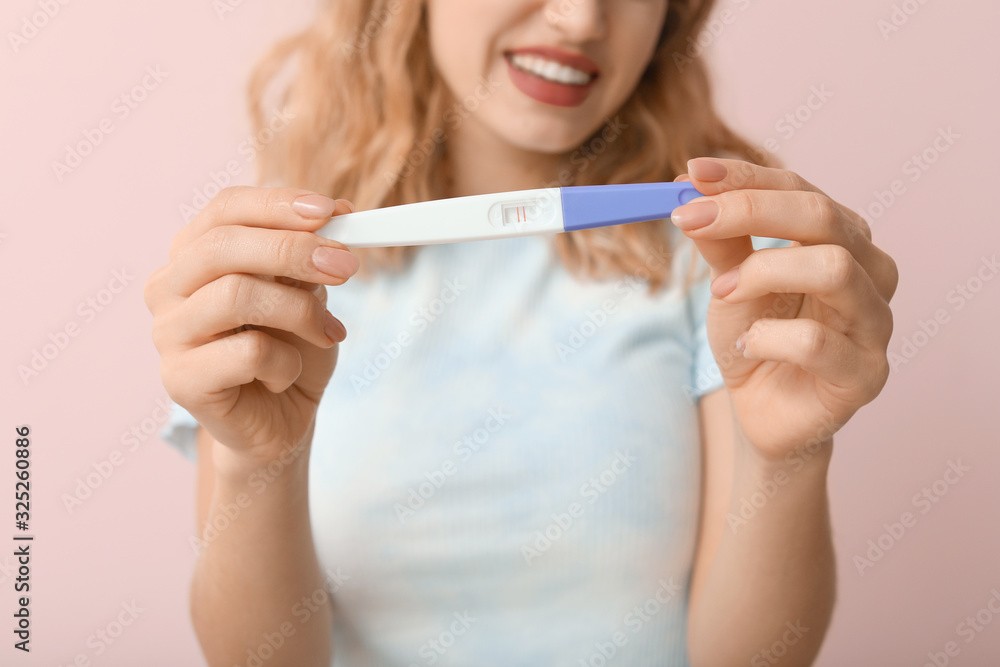 Happy young woman with pregnancy test on color background, closeup