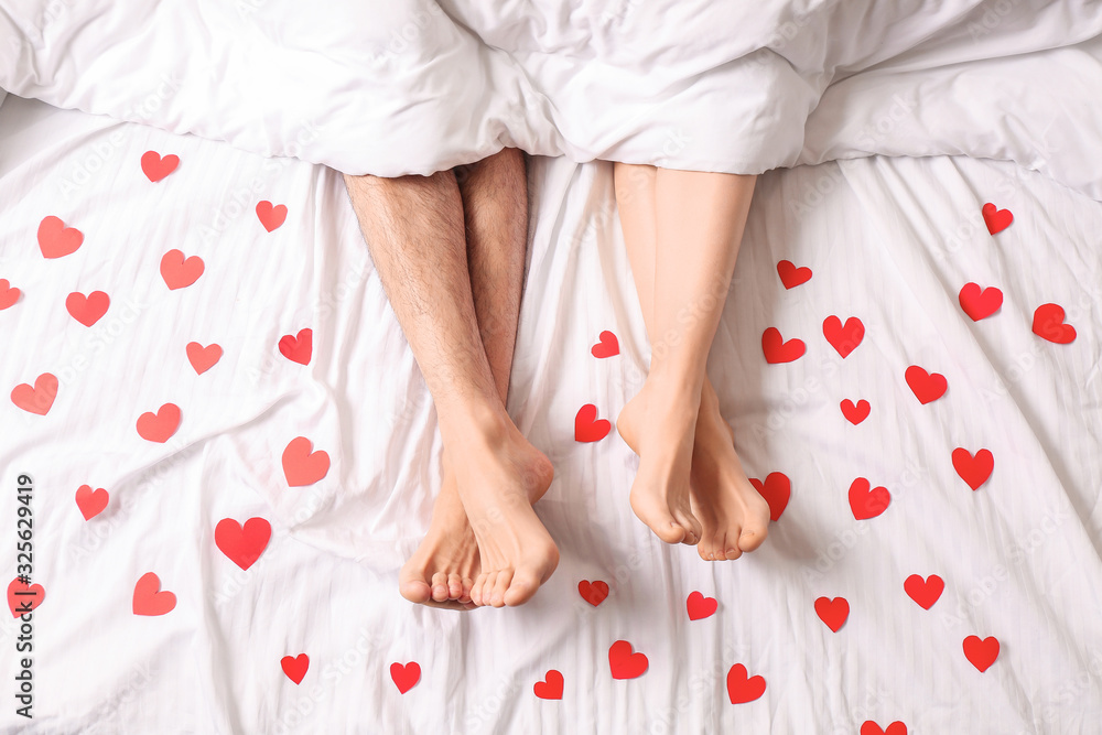 Young couple with red hearts lying in bed, top view