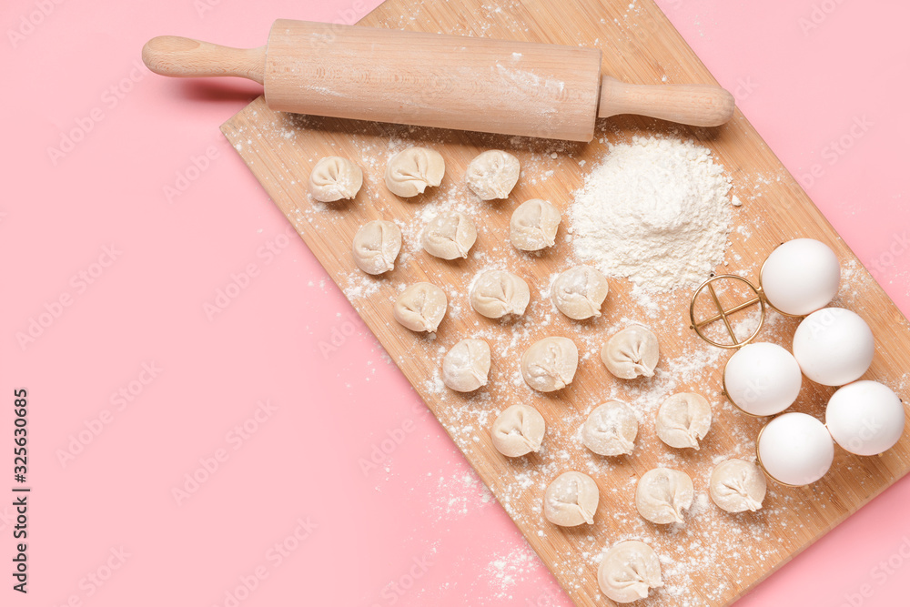 Raw fresh dumplings with rolling pin and eggs on color background