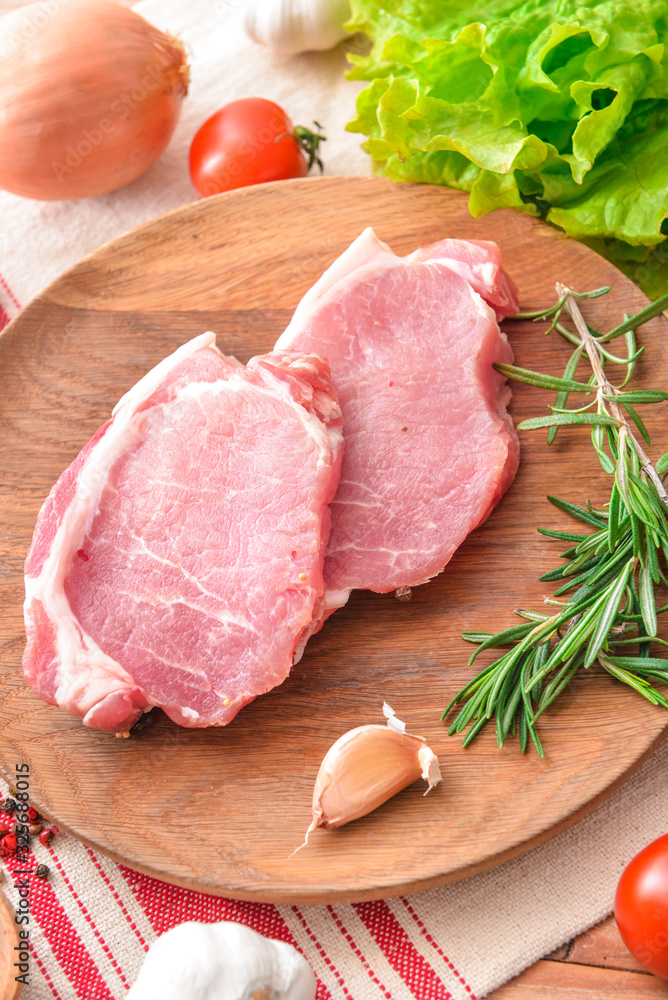 Plate with raw pork meat and vegetables on table