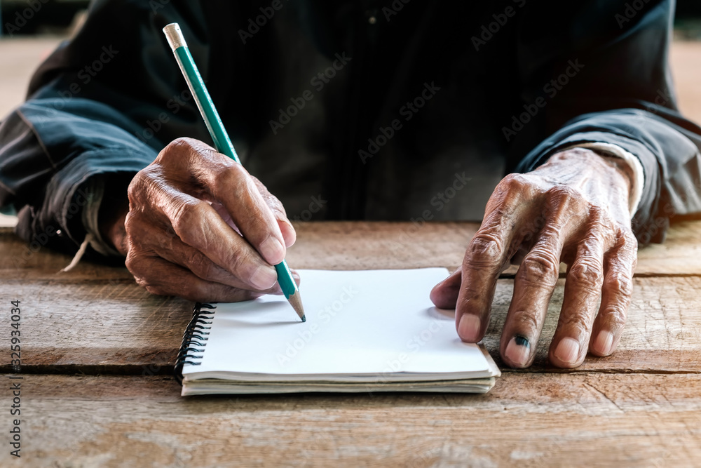 old man writing with a pencil in a notebook,Handwriting on the wood desk