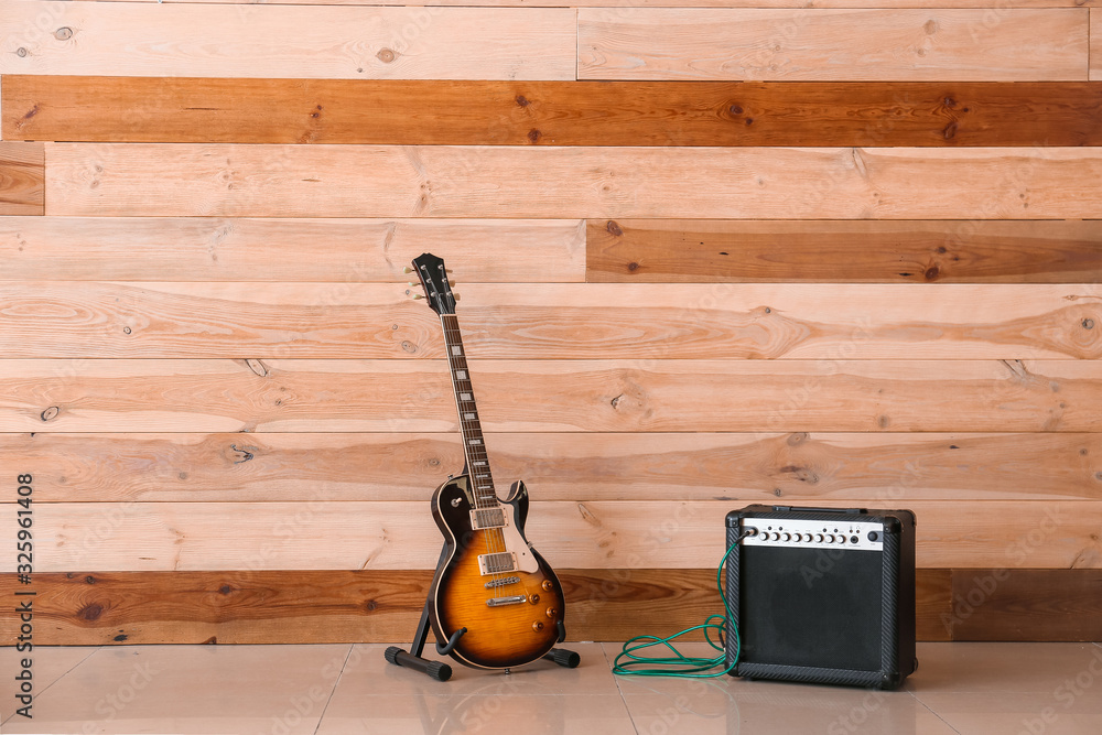 Modern guitar and amplifier near wooden wall