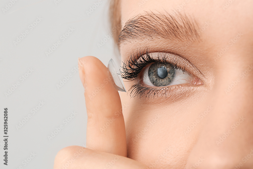 Young woman with contact lens on grey background, closeup