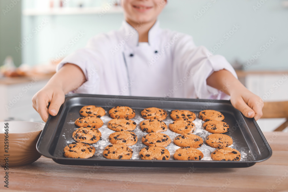 Cute little chef with cookies in kitchen