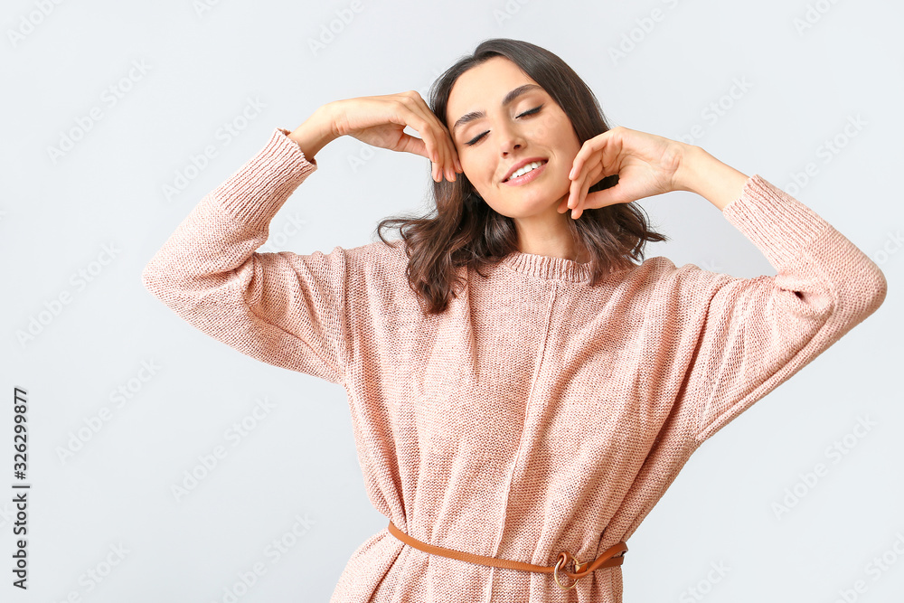 Beautiful young woman in warm sweater on light background