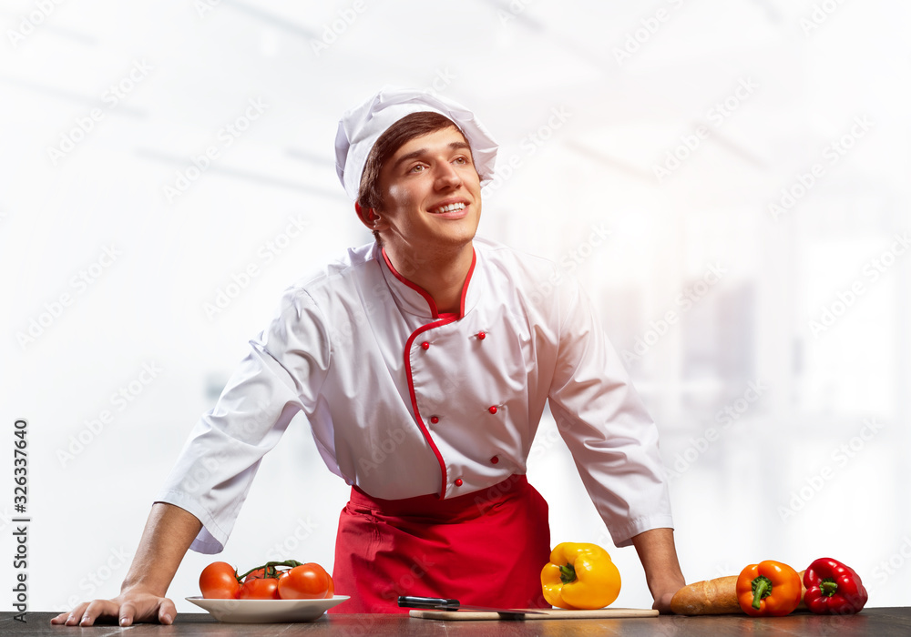 Young smiling chef standing near cooking table