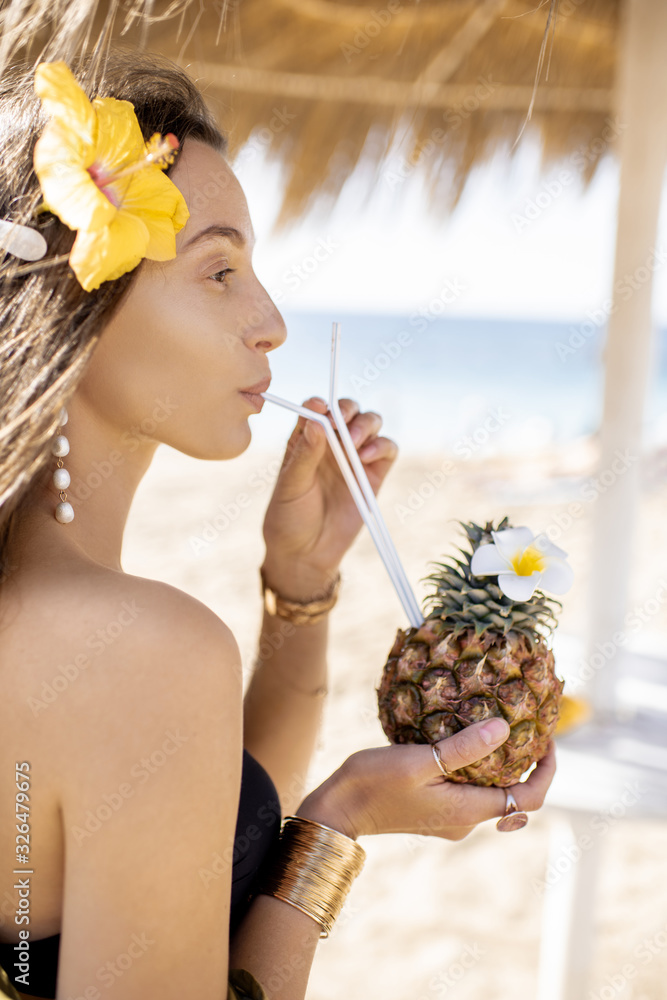 阳光明媚的一天，一位年轻漂亮的女士在海滩度假胜地喝着异国情调的鸡尾酒。概念