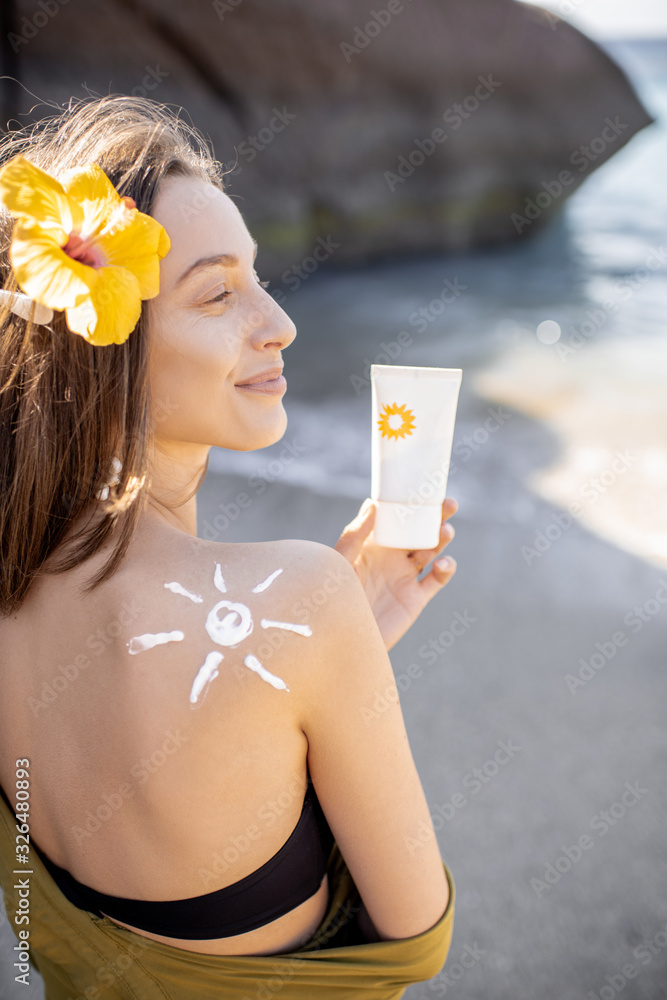 Portrait of a beautiful young woman with sun shape on her shoulder holding tube with sunscreen lotio