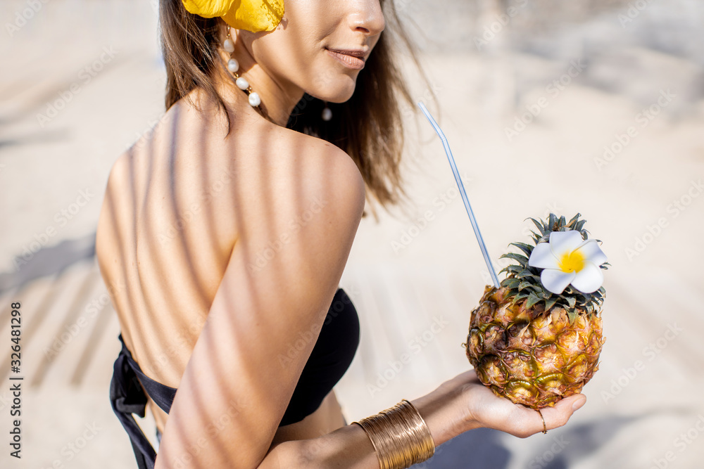 Portrait of a cute summer girl with exotic fruit shaded with palm leaves on the sandy beach