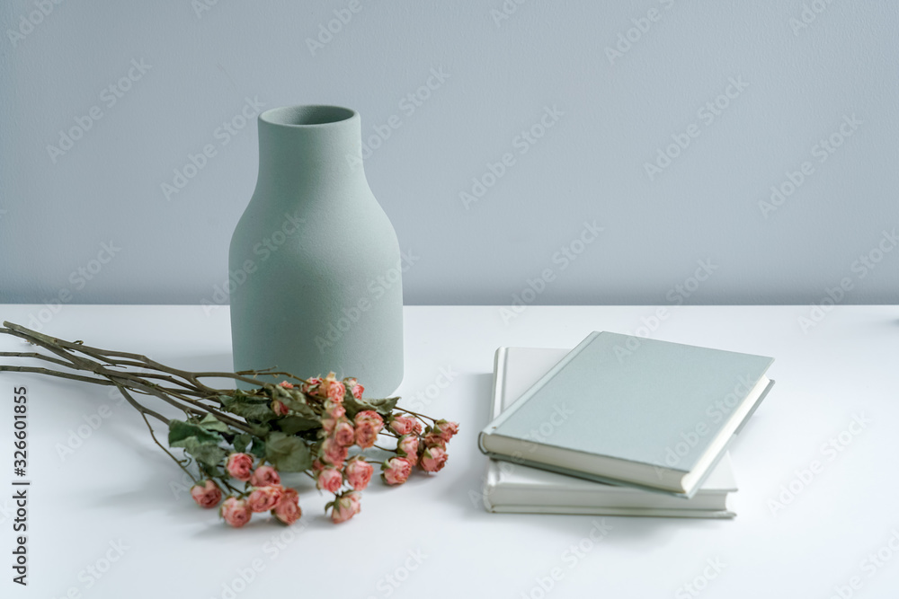 There are pink roses in the vase on the white desk, as well as books and notebooks