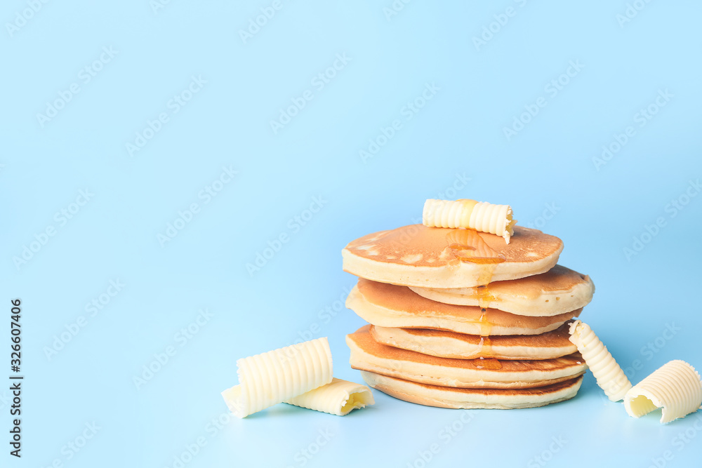 Tasty pancakes with honey and butter on color background