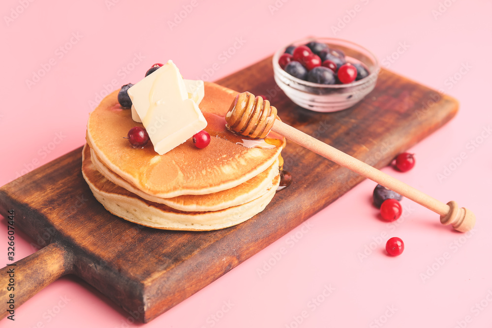 Tasty pancakes with honey, butter and berries on color background