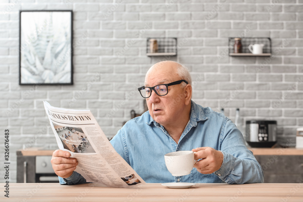 Portrait of elderly man drinking tea while reading newspaper at home