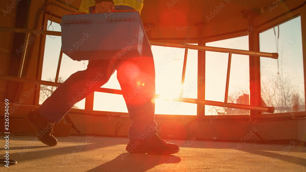 LENS FLARE Worker coming to work carries his toolbox and ladder across the room.