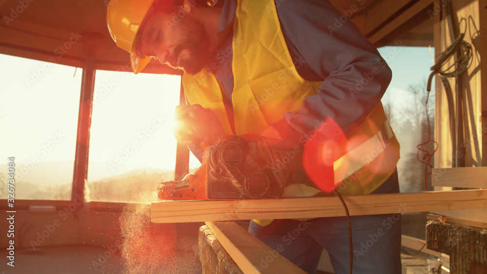 CLOSE UP: Golden sunbeams shine through the window as worker sands a long board.