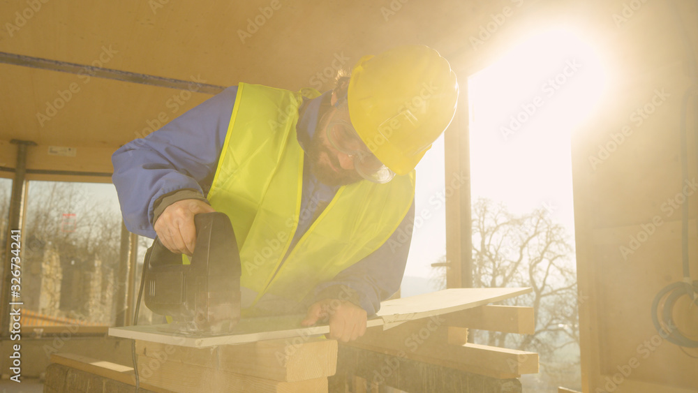 LENS FLARE: Builder working in a CLT house cuts a gypsum wall panel with jigsaw.