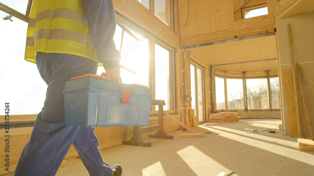 CLOSE UP: Unrecognizable builder arrives to work carrying his toolbox and ladder