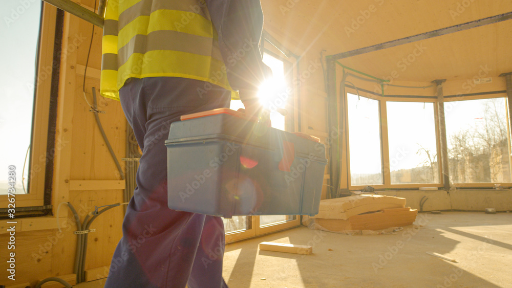 CLOSE UP: Golden sunbeams shine on worker coming to work in prefabricated house.