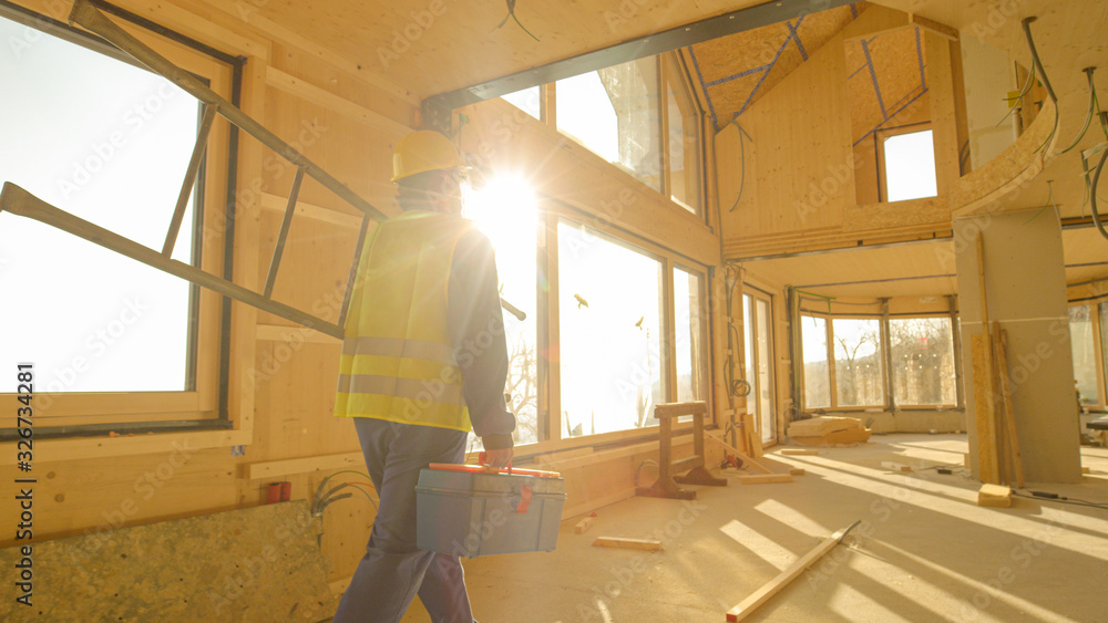 CLOSE UP: Golden sunbeams shine on worker coming to work in prefabricated house