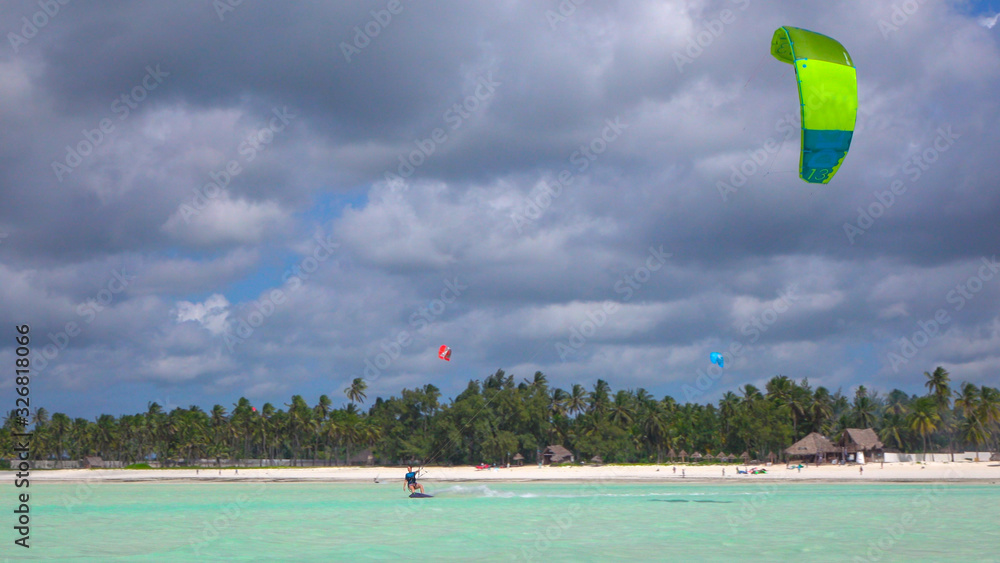 Female kiteboarder kiting in perfect blue lagoon in front of exotic sandy beach