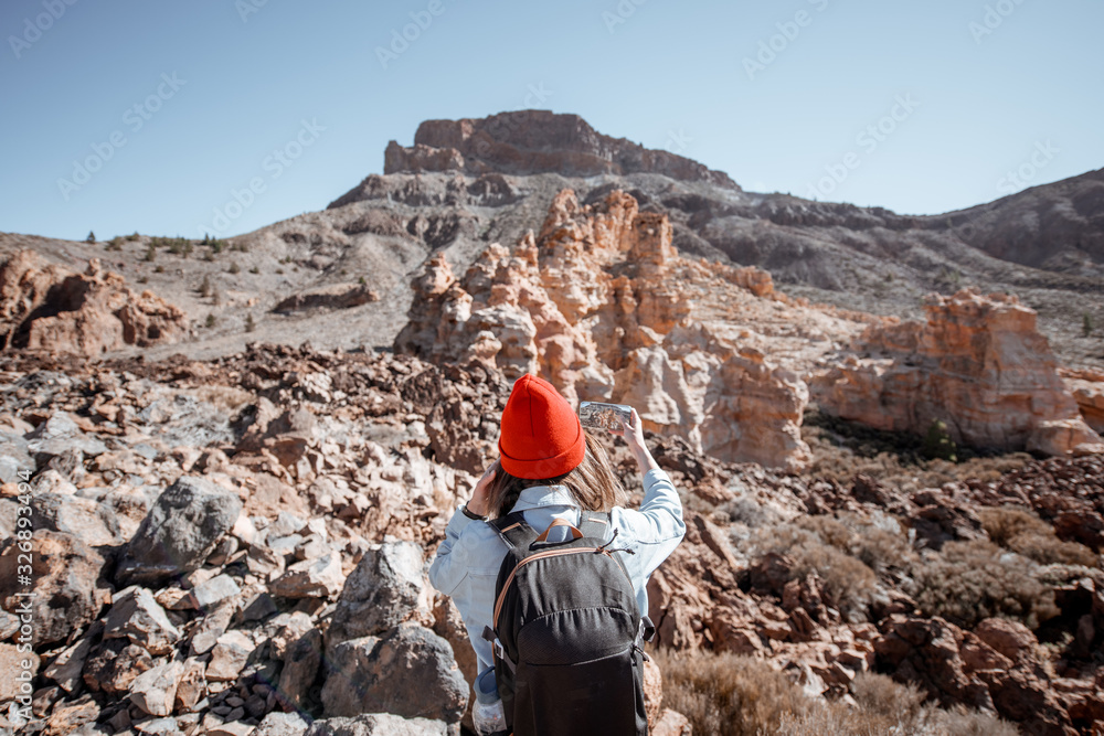 戴着红帽子、背着背包的年轻旅行者在d上旅行时用手机拍摄岩石景观