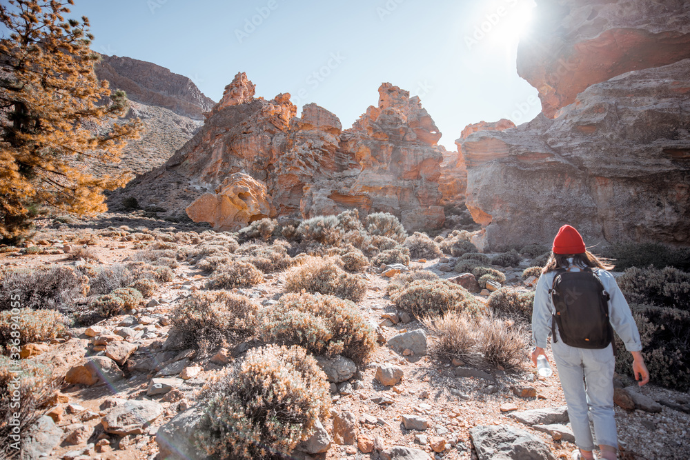 阳光明媚时，年轻的女性旅行者在巨石和火山之间的岩石地形上行走