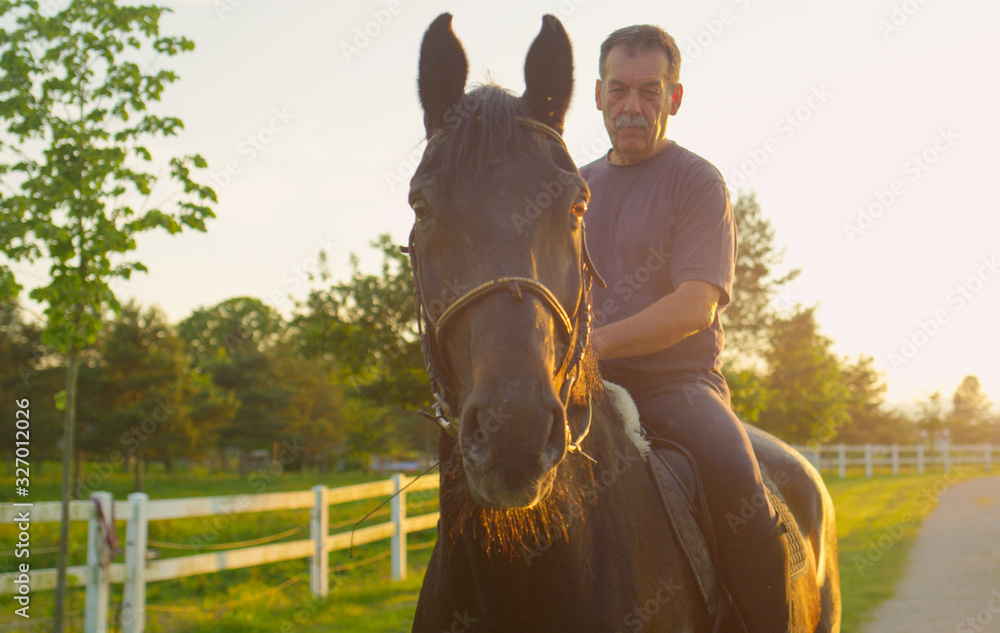 CLOSE UP: Senior cowboy sitting on strong horse and enjoying time at sunrise