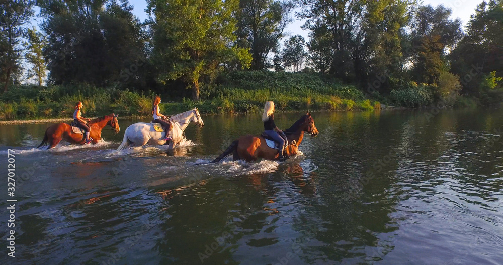 CLOSE UP: Three cheerful girlfriends riding horses in the river on sunny day